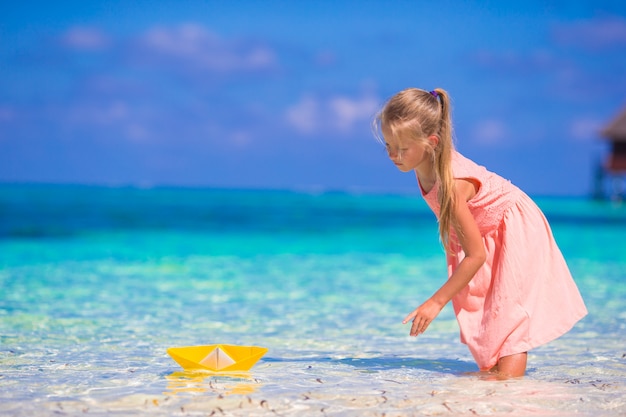 Adorable little girl playing with origami boat in turquoise sea