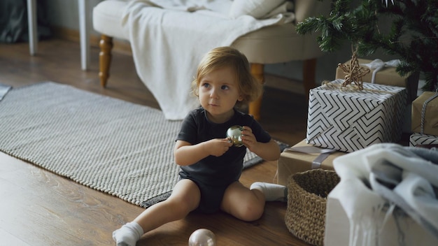 Adorable little girl playing with toy balls sitting near Christmas tree at home