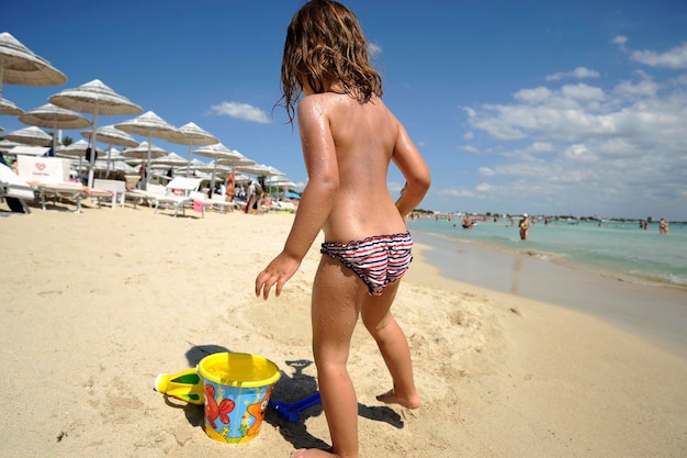 トロピカルビーチでおもちゃで遊ぶ愛らしい少女家族の夏休み小さな子供たちと一緒に旅行子供たちの夏とスキンケアのコンセプト