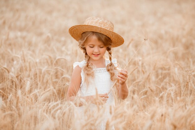 Adorabile bambina gioca su un campo di grano in una calda giornata estiva