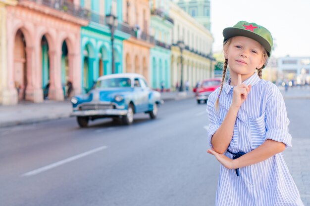 Adorabile bambina nella zona popolare di l'avana vecchia, cuba. ritratto di bambino, auto d'epoca classica americana