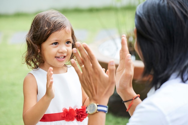 Adorable little girl in puffy dress clapping hands with father when they are playing outdoors
