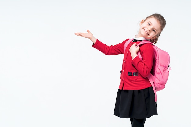 Adorable little girl in red school jacket, black dress, backpack pointing