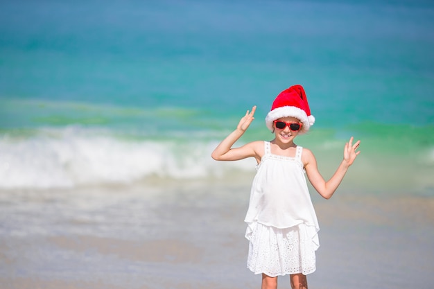 Adorable little girl in Santa hat on tropical beach