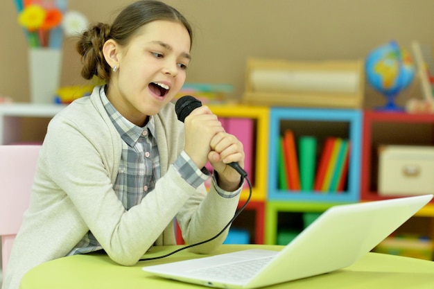 Adorable little girl singing karaoke with modern laptop at home