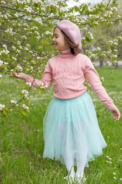 사랑스러운 어린 소녀는 공원에서 피는 하얀 사과 나무 옆에 서 있다