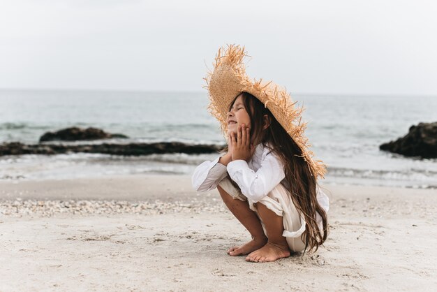 Photo adorable little girl in straw hat at beach during summer vacation