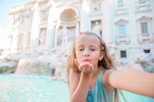 Adorable little girl taking selfie by the Fountain of Trevi in Rome.