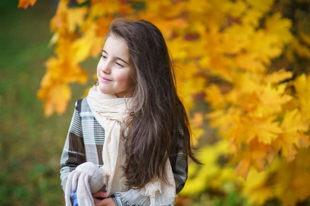 Adorabile bambina con foglie di autunno nel parco di bellezza