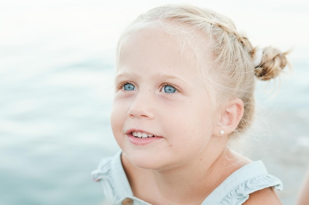 Adorable little girl with blue eyes looking away near blurred sea at beach during summer vacation