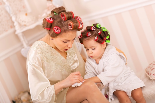 Adorable little girl with her mother in curlers paint their fingernails. Copies mom's behavior. Mom teaches her daughter to take care of herself. Beauty day.