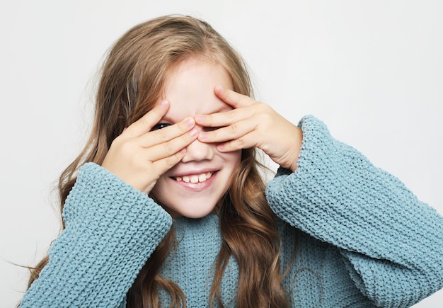 Adorable little girl with long curly blond hair closes her eyes with her palm