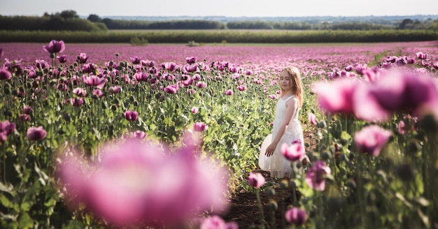 Photo adorable little girl with long hair in white dress lonely walking in the lilac poppy flowers field