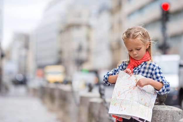 Adorable little girl with map of european city outdoors