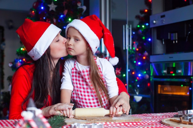 Bambina adorabile con la madre che porta i cappelli di santa che cuociono insieme i biscotti del pan di zenzero di natale