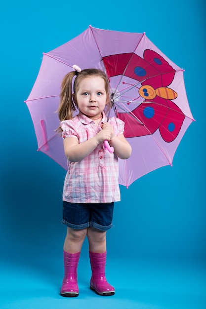 Bambina adorabile con l'ombrello rosa su fondo blu