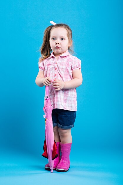 Adorable little girl with pink umbrella on blue background