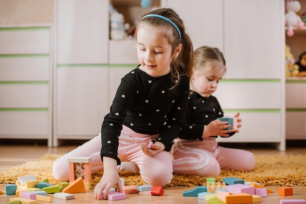 Adorable little girls are playing with colored blocks at home