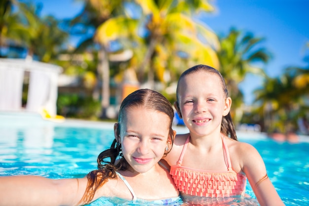 Adorable little girls playing in outdoor swimming pool. Cute kids take selfie.