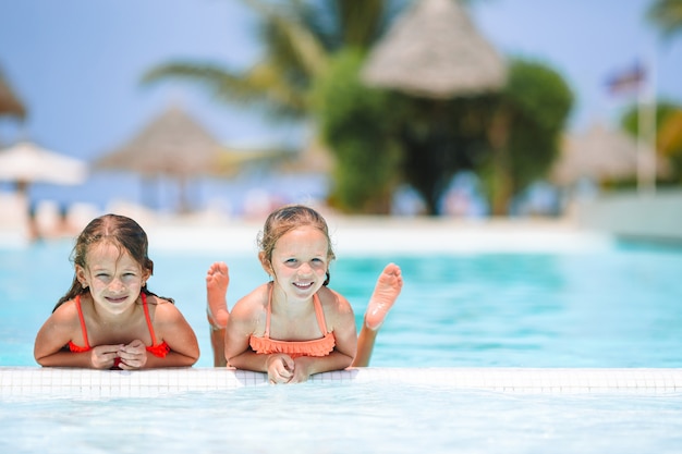 Adorable little girls playing in outdoor swimming pool on vacation