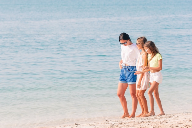 Прелестные маленькие девочки и молодая мать на тропическом белом пляже