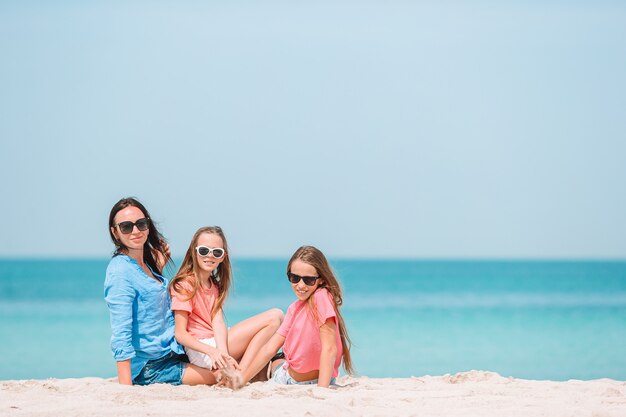 Adorable little girls and young mother on white beach