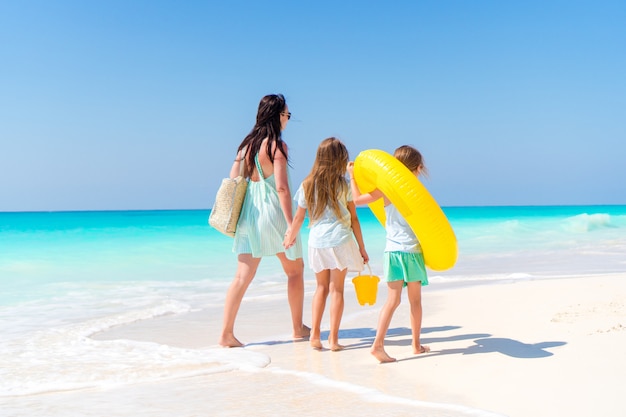 Adorable little girls and young mother on white beach.