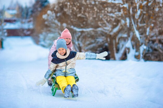 Adorable little happy girls sledding in winter snowy day