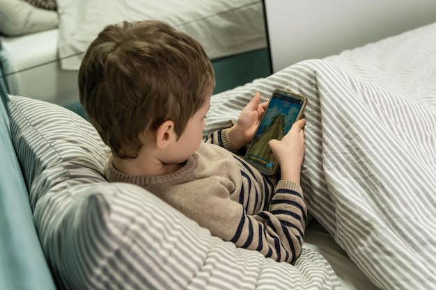 Adorable little kid using smartphone child playing video game