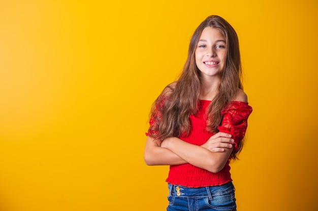 Adorable little pre teen girl on yellow background smiling with arms crossed.