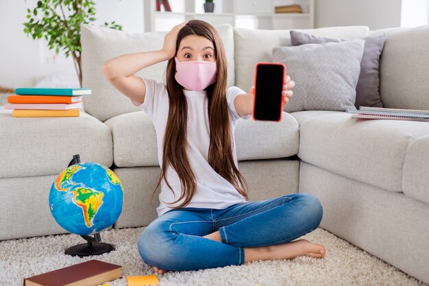 adorable little schoolgirl in medical mask hold telephone device