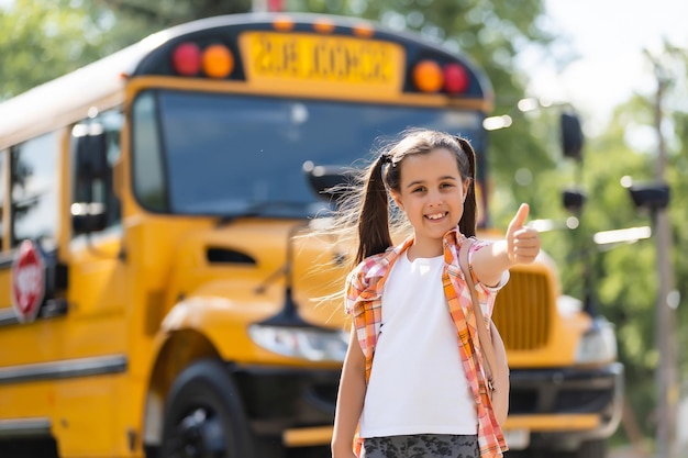 adorable little schoolgirl near school bus and looking at camera