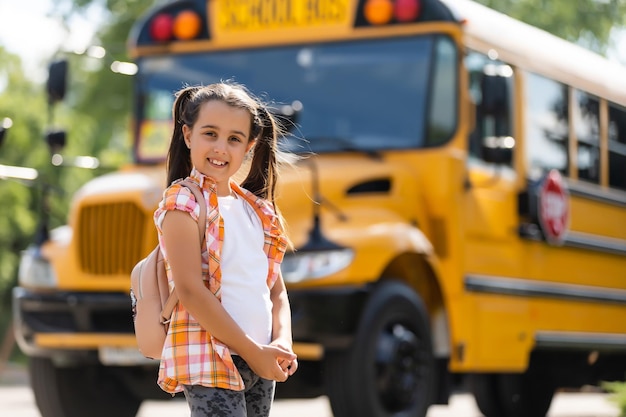 adorable little schoolgirl near school bus and looking at camera