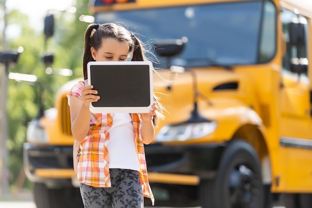 adorable little schoolgirl near school bus and looking at camera