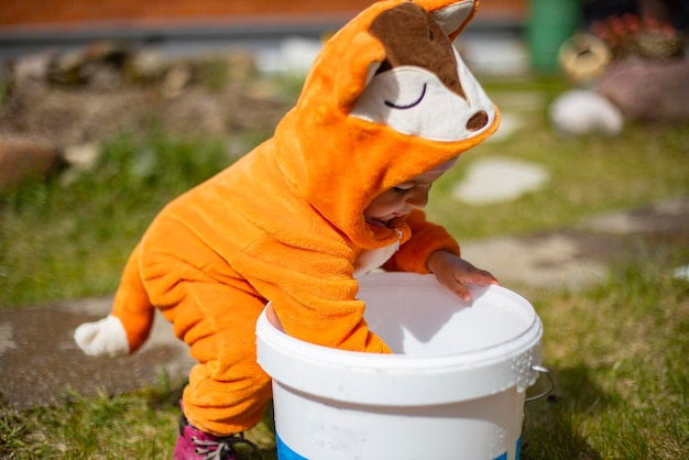 Фото Очаровательный маленький малыш, играющий с водой на заднем дворе в солнечном свете, ребенок в костюме лисы