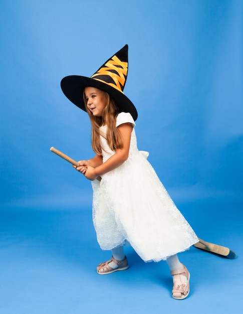 Adorable little witch in a white dress flies on a broomstick isolated on a blue background.