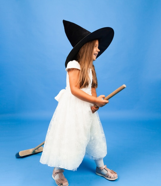 Adorable little witch in a white dress flies on a broomstick isolated on a blue background