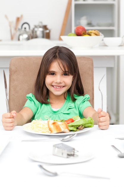 パスタとサラダを食べるためにフォークを持って愛らしい小さな女の子