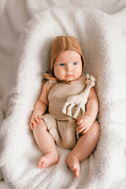 Adorable lovely newborn male baby with smiling happy face lifestyle portrait from above. Funny infant child lying with toy in basket covered with white bedspread.