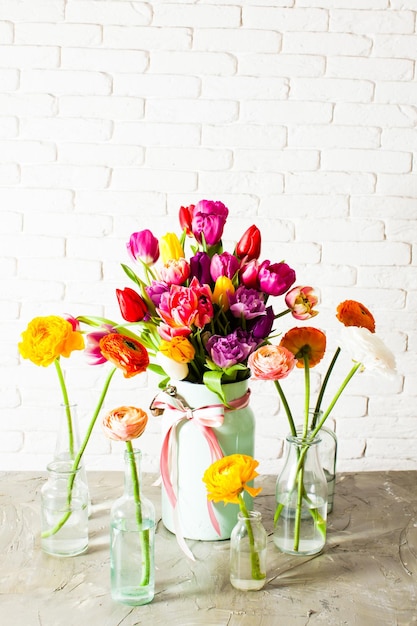 Adorable multicolor bouquet made from bright cheerful tulips, put in metal can. Several glass bottles with ranunculus flowers standing around. White background