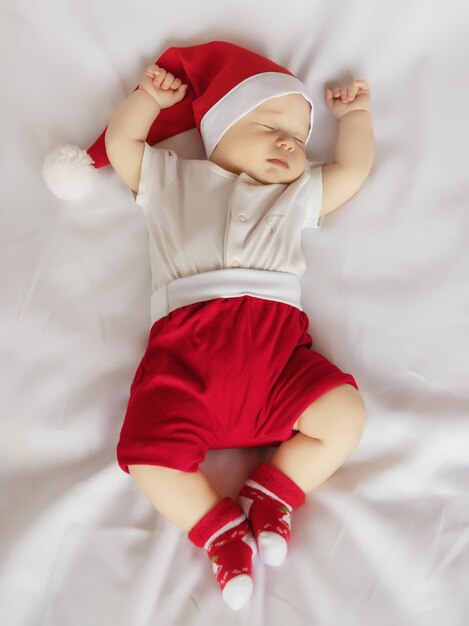 Adorable newborn baby in Christmas Santa Claus costume sleeping on white sheet