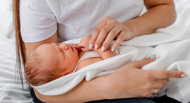 母親の手で眠っている愛らしい新生児。ママと昼寝幼児の子供のクローズアップの肖像画。屋内で子供を気遣う女の子