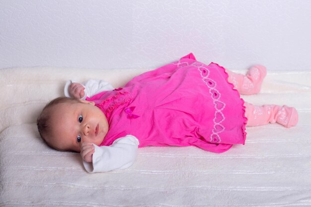 Photo adorable one month old baby girl in pink dress lies on a soft blanket