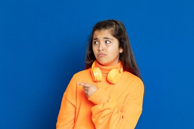 Adorable Preteen girl with yellow jersey gesturing over blue wall