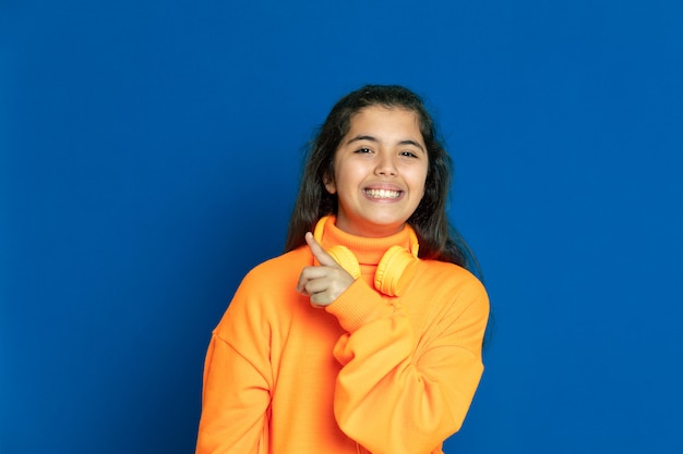 Adorable preteen girl with yellow jersey gesturing over blue wall