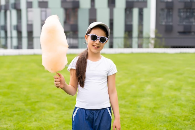甘い綿菓子を食べている愛らしい、かなり巻き毛の少女。幸せな子供、夏や春に公園で感情と綿菓子を食べる子供。