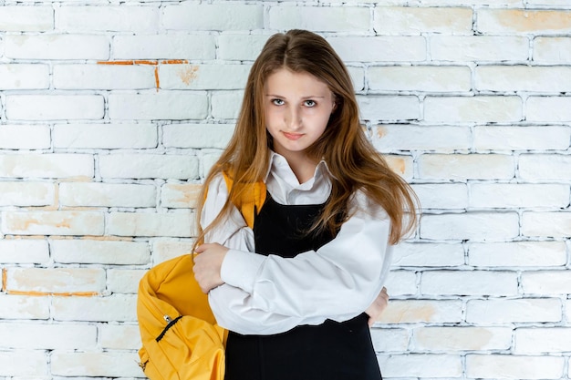 Adorable schoolgirl stands on white background and crossed her arms