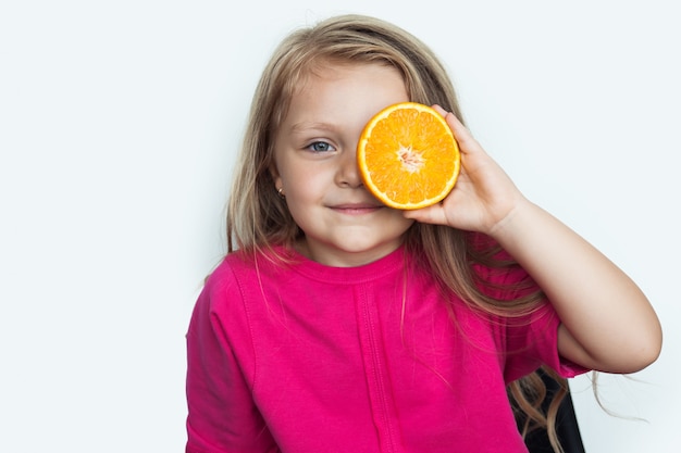 Photo adorable small girl is covering her eye with an orange on white