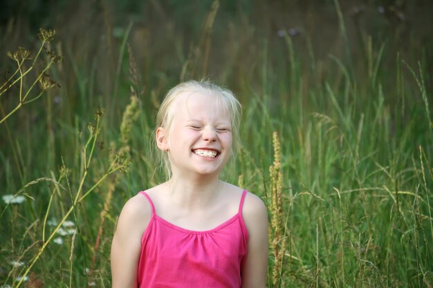 Adorabile ragazza bionda sorridente in abito luminoso in stile etnico che cammina nel campo verde in estate