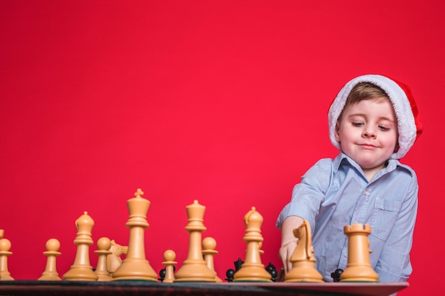 Foto adorabile ragazzino sorridente che indossa il cappello di natale e gioca a scacchi.